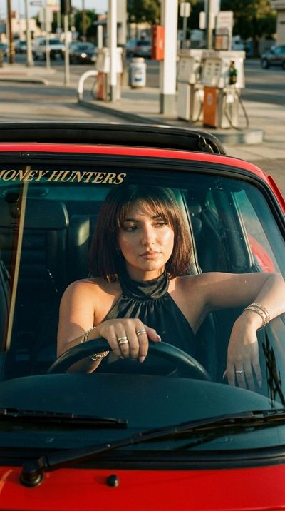 A confident woman in a vintage red car at golden hour