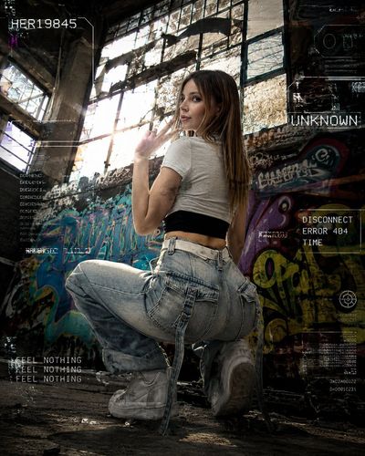 Urban grunge model poses by graffiti window in abandoned warehouse