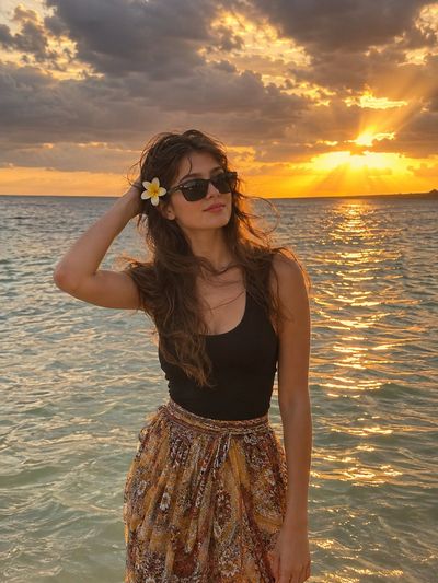 Woman at sunset beach with wind-tousled hair and plumeria