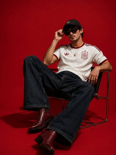 A stylish young man in a red studio sits confidently in a black lounge chair.