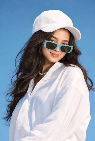 A woman in turquoise sunglasses poses under a clear blue sky.