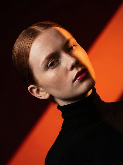 Model in black turtleneck poses against vivid orange and burgundy panels
