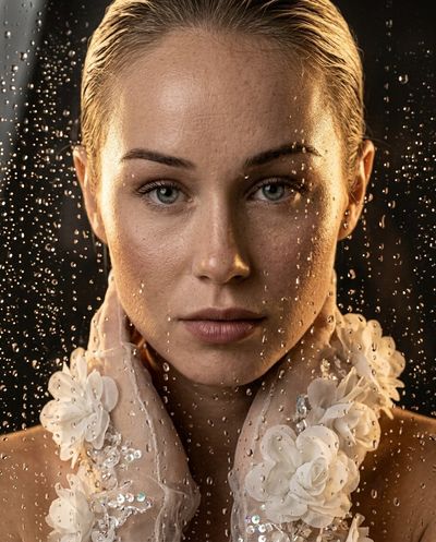 Young woman behind rain-streaked glass with golden glow and tulle gloves