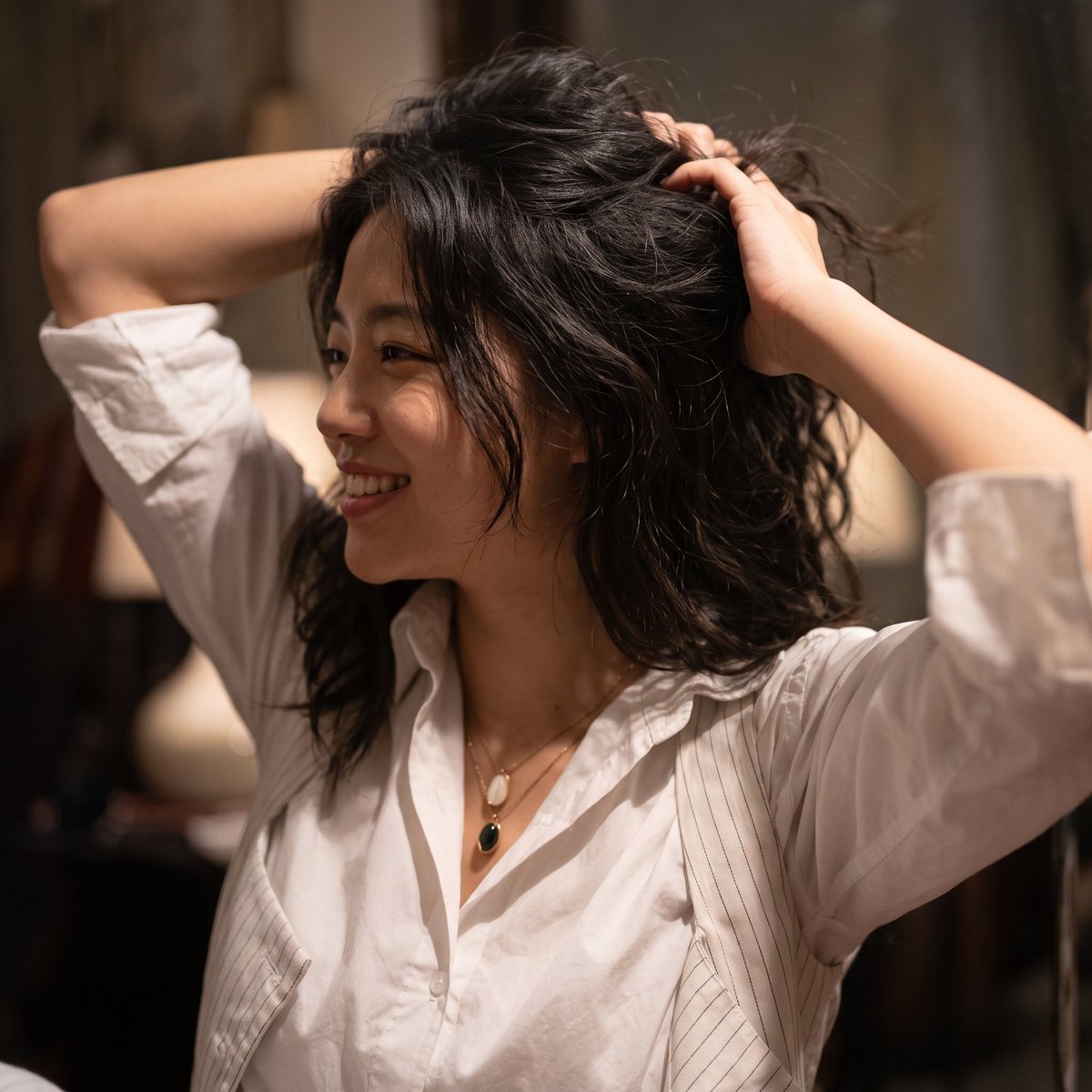 A South Asian woman gathers her hair in a sunlit candid portrait