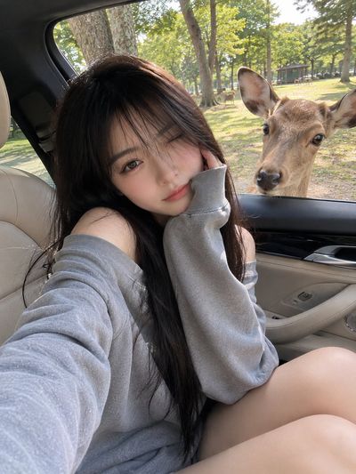 Girl makes peace sign while deer peers into luxury car