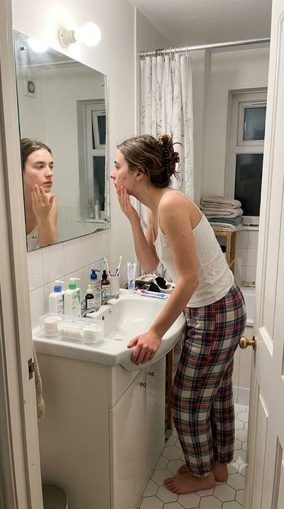 Young woman applies moisturizer in harsh bathroom light captured candidly