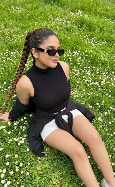A slender man sits on lush grass among daisies