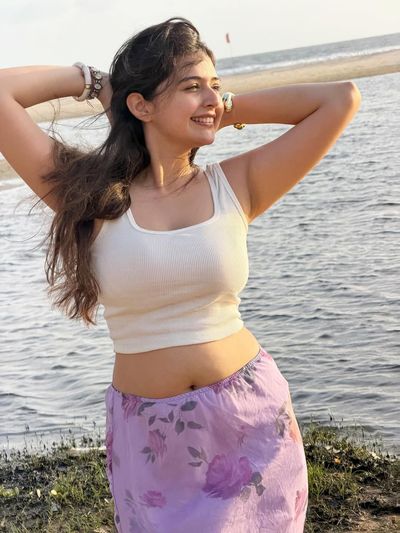 Indian woman in white crop top smiles at golden hour beach