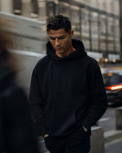 A man in an oversized black hoodie walks through a busy city street.