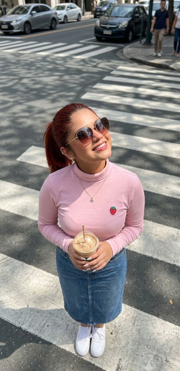 Woman in pink T-shirt holds iced coffee at zebra crossing