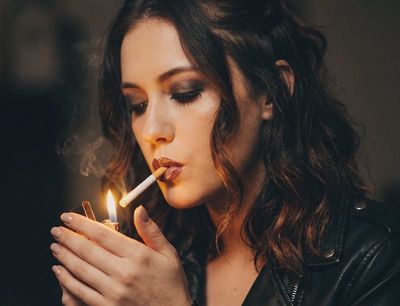 Woman lights a cigarette with a warm flame in darkness