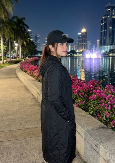 Young woman in Nike cap smiles softly by glowing city river