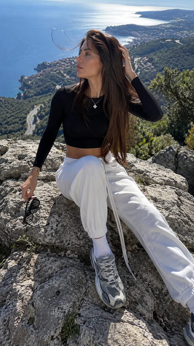 Young woman sits on coastal rock with windblown hair and distant sea