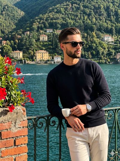 Man in sunglasses poses on balcony with espresso and lake view