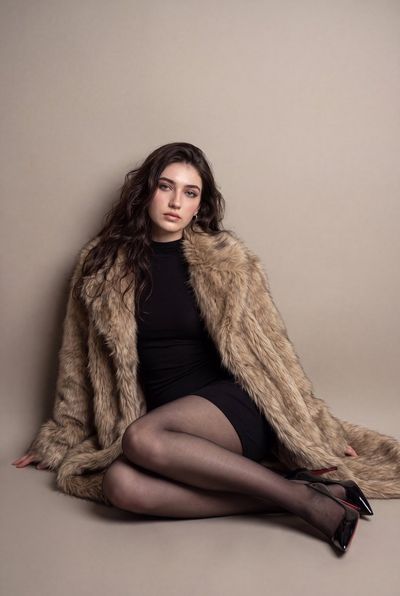 A model sits on the floor in a warm studio wearing a fur coat.