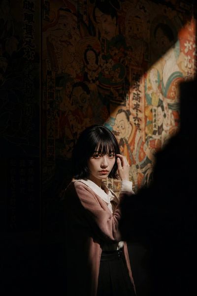 Woman in vintage jacket stands in dark room with mural