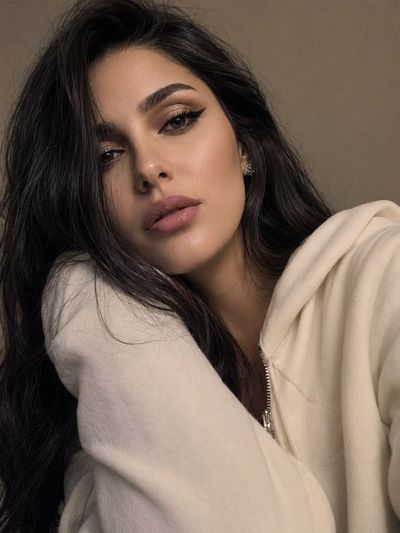A girl in a cream hoodie tilts her head in a soft selfie