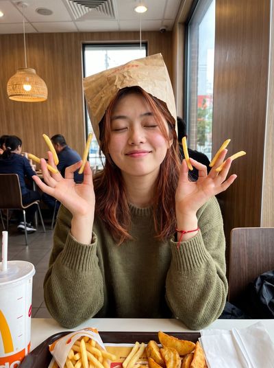 Woman Crowned with Paper Bag Smiles Holding Fries Like Cigarettes