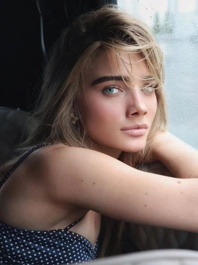 Young woman with blue-green eyes sits in vintage car looking at camera