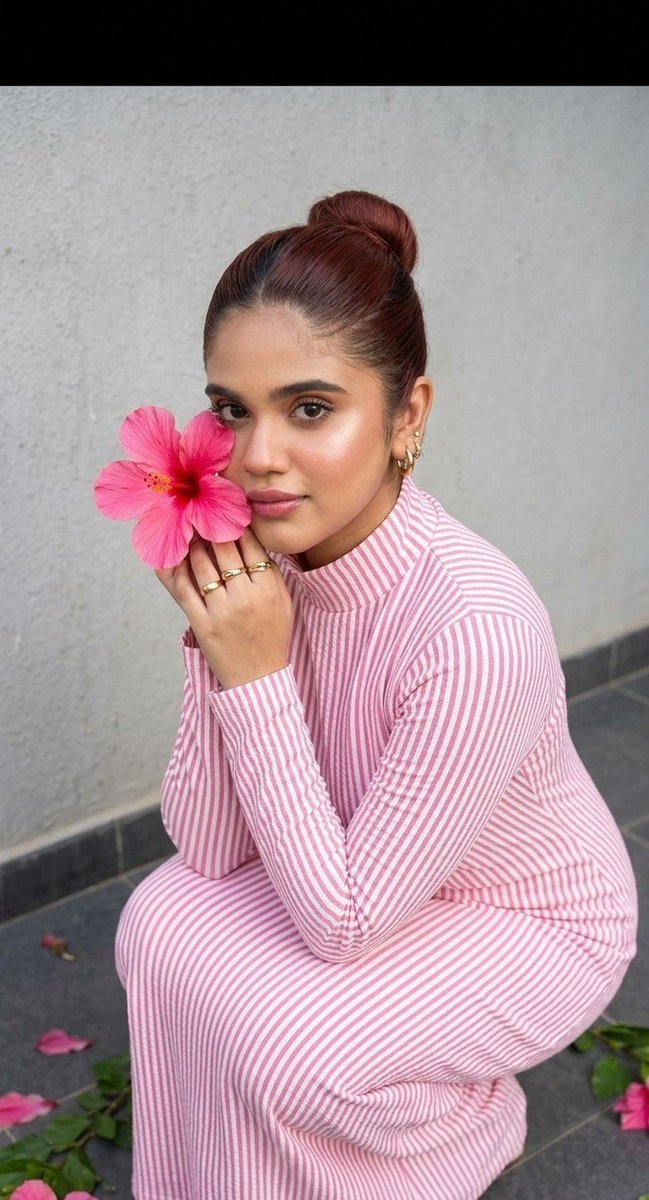 A girl in a pink striped dress presses a hibiscus to her cheek.