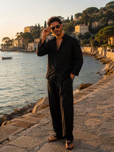 A stylish man adjusts his sunglasses on a sunset promenade