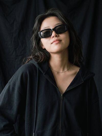 Confident East Asian Woman in Chunky Sunglasses Gazes Upward in Studio