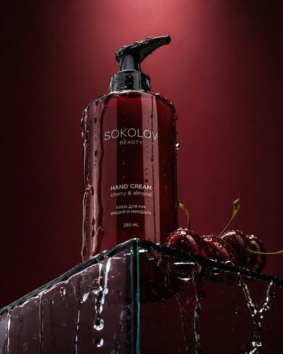 Sokolov dark red hand cream bottle drips water on glass podium with cherries