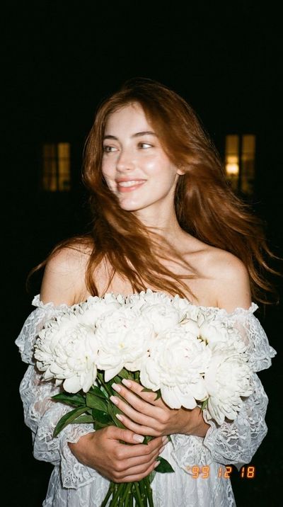 Girl with white peonies turns away under harsh flash in dark garden