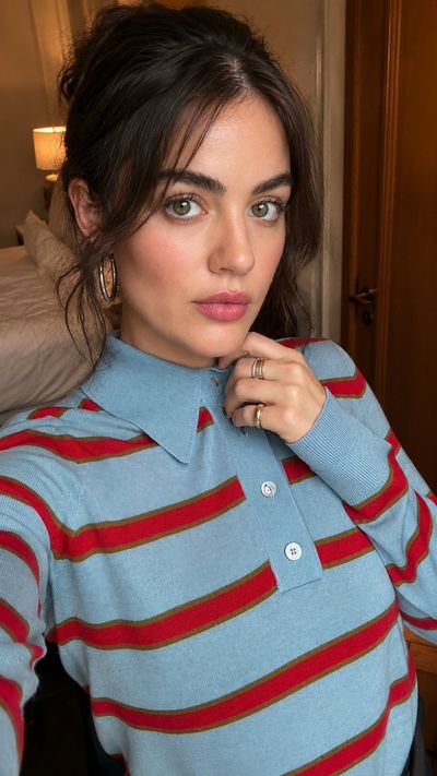 A young woman takes a selfie in a cozy hotel room wearing a striped sweater.