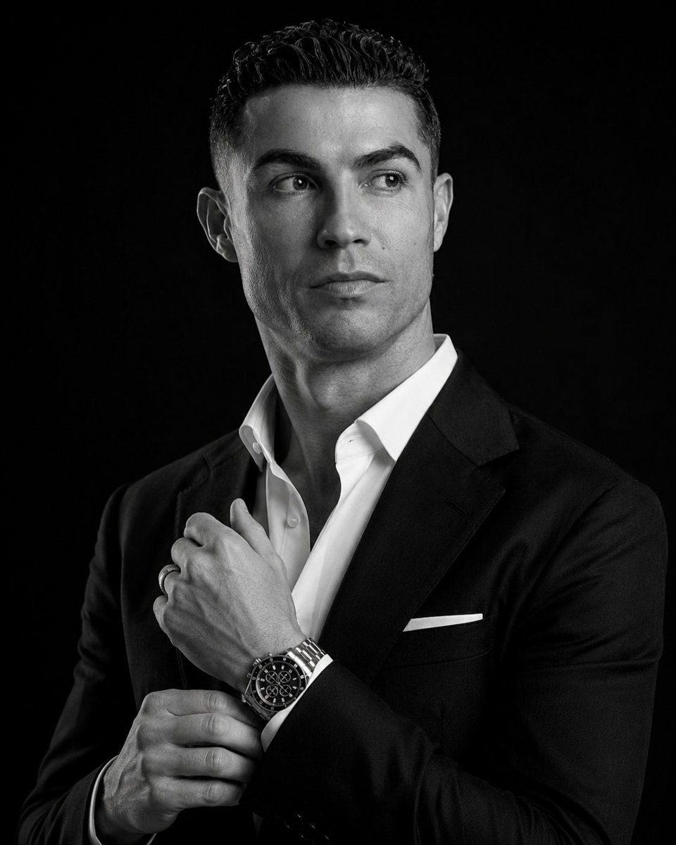 A man in a tailored suit adjusts his watch in dramatic light