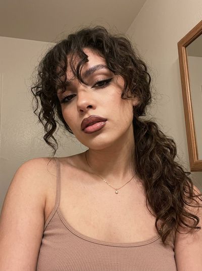 Low-angle selfie captures Y2K curly-haired woman with glossy lips and cat-eye