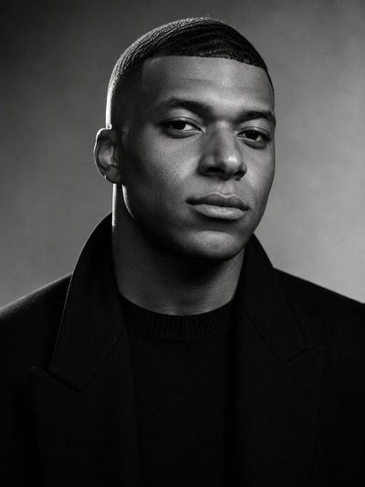 Confident athlete in black overcoat stares with calm determination.