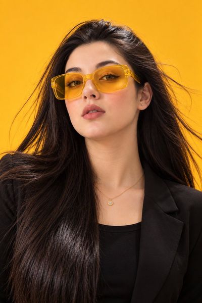Confident woman in yellow sunglasses poses against mustard backdrop