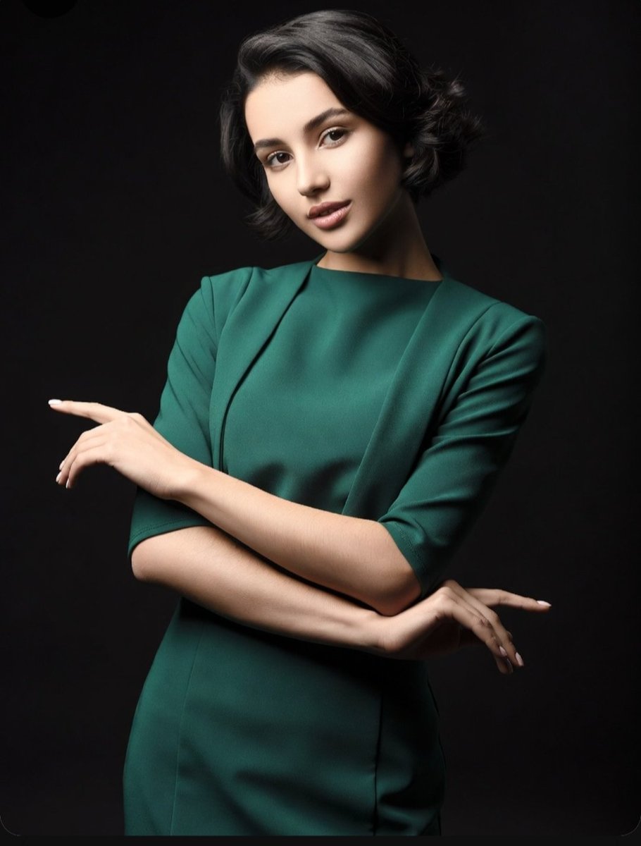 Elegant woman in green dress crosses arms in studio portrait