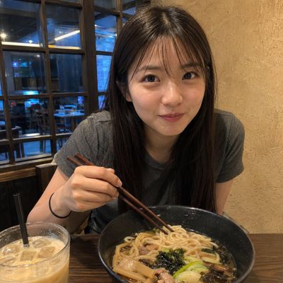 A shy young woman pauses with chopsticks over her steaming noodle bowl