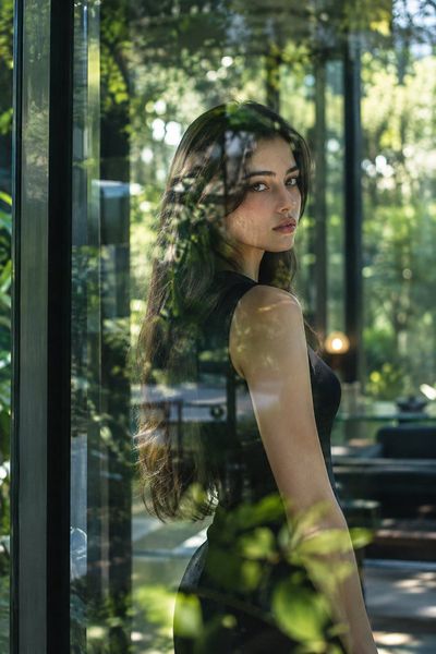 Woman in black dress stands behind lush green reflective glass window