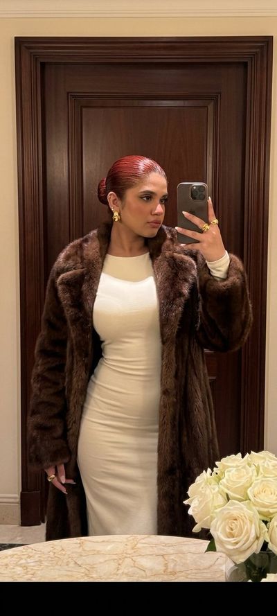 Woman in fur coat checks her reflection in classic interior