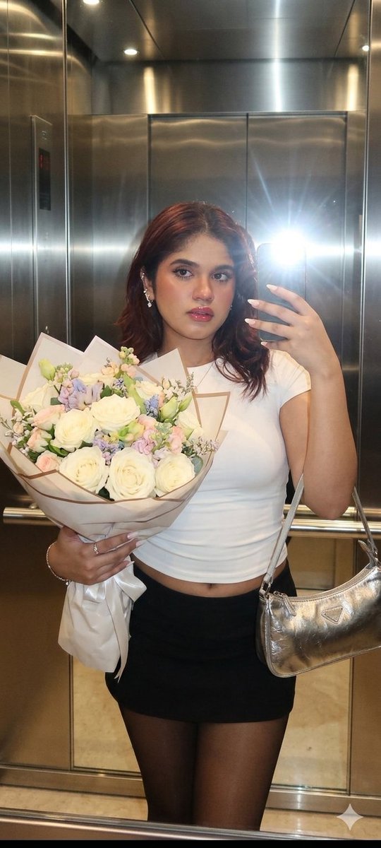 A woman holds a bouquet in a mirrored elevator at night