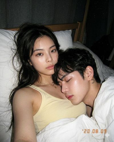 A couple lies intimately in dim bedroom lighting from above