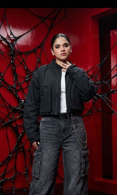 A stylish young woman wears oversized black streetwear in a dark studio.