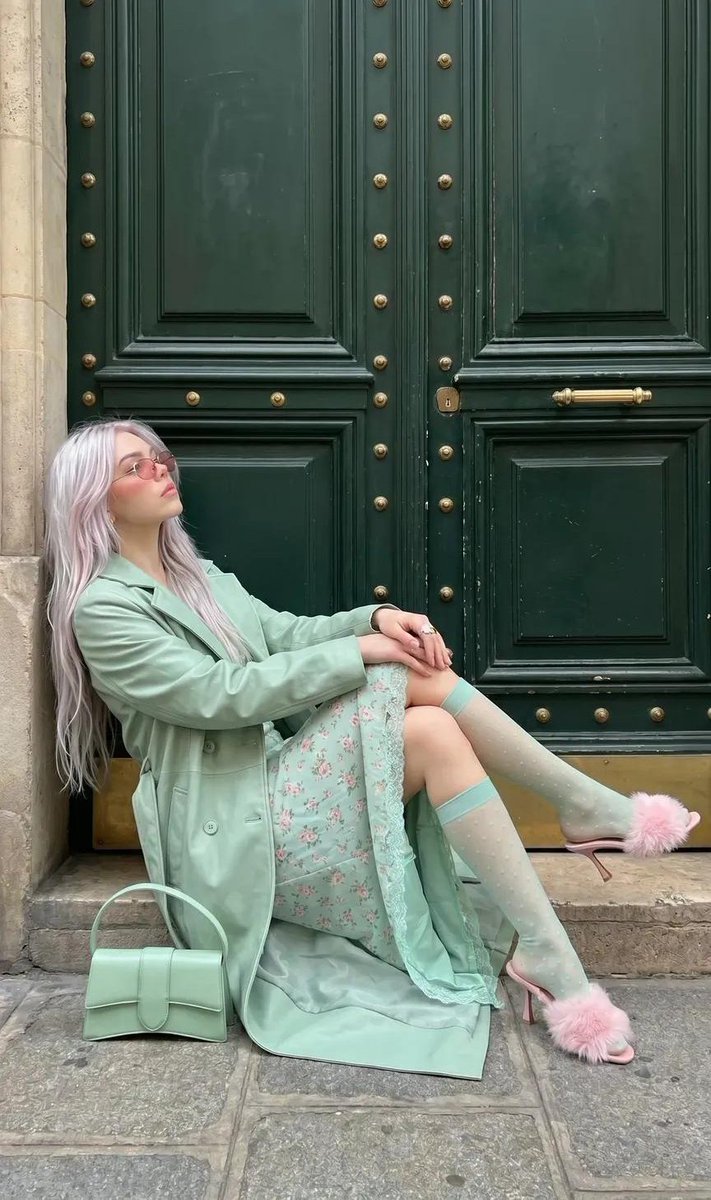 A platinum-haired woman in mint fashion poses by a grand green door