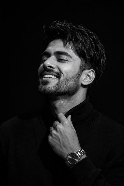 A man in black turtleneck smiles softly under dramatic light