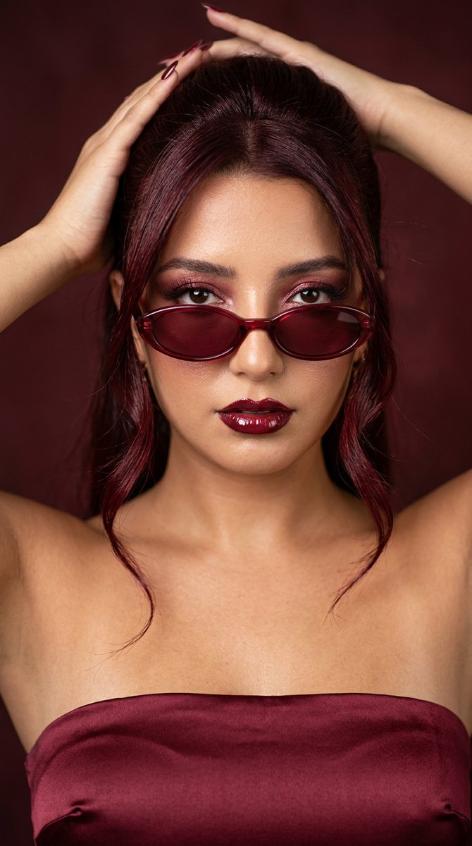 Woman in wine-red glasses sweeps back glossy hair in editorial shot