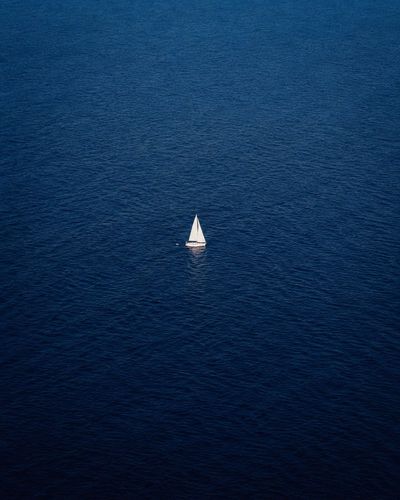 A solitary white sailboat drifts on an endless blue ocean