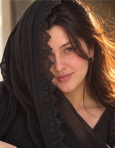 Elegant woman in black lace dupatta smiles in golden light