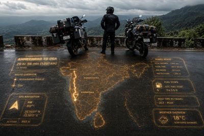 Adventure motorcyclists pause at golden HUD map overlook in India.