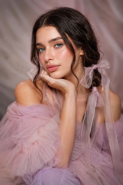 Woman with blue-green eyes rests chin on hand in pastel gown