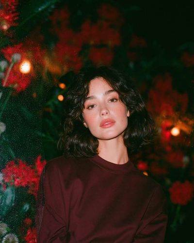 Rain-speckled window frames melancholic woman in crimson garden at night
