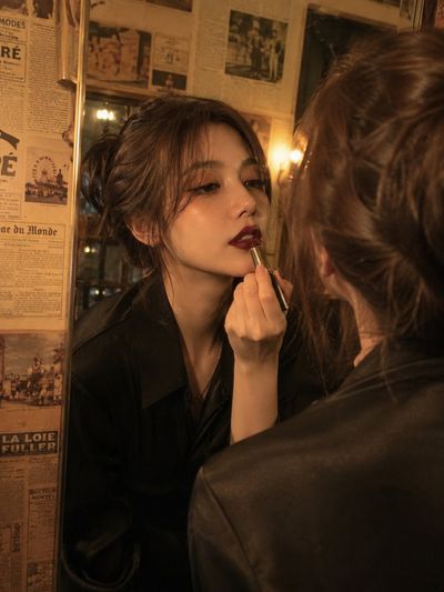 A woman applies deep burgundy lipstick in a vintage mirrored dressing room