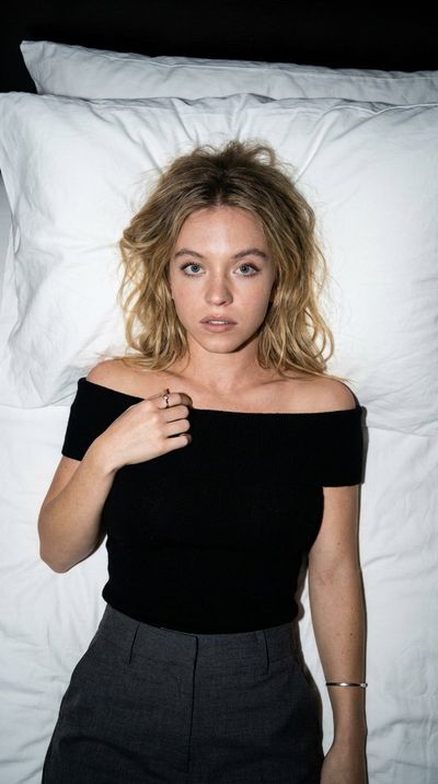 A woman lies on white sheets under stark flash light